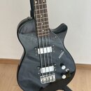Černá elektrická basová kytara s hnědým hmatníkem a dvěma bílými snímači. Na černém plechu je viditelný nápis GRETSCH. Nástroj je umístěn na černém s…