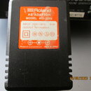 Černý síťový adaptér s oranžovou nálepkou. Na nálepce je uveden nápis Roland AC ADAPTOR MODEL ACI-220J, INPUT 220V~50Hz 18 VA a OUTPUT 9V⎓1000mA. Dol…
