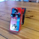 Červený kytarový efekt s nápisem Subnup a pod ním menším textem BASS OCTAVER. Na horní straně jsou tři černé otočné oválné knoflíky s popisky DRY, SU…