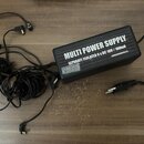 Černý obdélníkový zdroj napájení s několika připojenými kabely a konektory. Na horní straně je bílý nápis MULTI POWER SUPPLY a pod ním text SEPARATE…