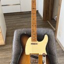 Elektrická kytara s tónem sunburst, krčkem a hmatníkem z přírodního dřeva. Na hlavě je viditelné logo Fender. Kytara má krémový pickguard a chromovan…