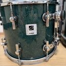 Tmavě zelený buben s výraznou strukturou dřeva a chromovaným kováním. Uprostřed korpusu je čtvercový štítek s nápisy „DESIGNER SERIES“, „MAPLE LIGHT…