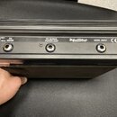 Zadní strana černého elektronického zařízení s chladičovými žebry. Jsou zde čtyři konektory a nápisy: „ONLY USE PSA 0812 DC-5V 500mA SERVICE 120V/230…
