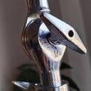 Detail chromovaného spojovacího kloubu stativu s černým knoflíkem nahoře. Na kovové části je vyryté logo připomínající stylizované písmeno S. Povrch…
