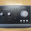 Šedý audio rozhraní s nápisy AUDIENT a iD14. Zařízení má velký ovládací knoflík, dva menší knoflíky s označením GAIN 0 10 u kanálů 1 a 2, dva přepína…