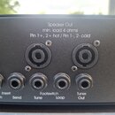 Detailní pohled na zadní panel černého hudebního zařízení s řadou konektorů. V horní části jsou dva XLR výstupy s nápisem „Speaker Out min. load 4 oh…