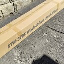 Fotografie zobrazuje dlouhý, úzký karton hnědé barvy položený na asfaltu u kamenné zdi. Na boku krabice je černý nápis STW-370S Winch-driven stand 37…