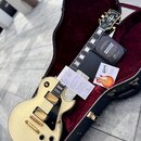 Bílá elektrická kytara typu Les Paul se zlatým hardwarem a černým pickguardem v černém kufru s červeným vnitřkem. Na hlavě hmatníku je nápis Gibson.…