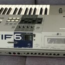 Stříbrný digitální klavír s nápisem MOTIF 6 a logem YAMAHA. Na zadní straně jsou viditelné různé konektory a přepínače s popisky jako OPTICAL OUTPUT,…