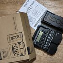 Na fotografii je černý kytarový efektový procesor Zoom G1X FOUR s integrovaným expresním pedálem. Vedle přístroje je umístěna jeho originální kartono…