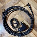 Černý pletený kabel s úhlovým konektorem na jedné straně a rovným konektorem na druhé. Na černé stahovací stisce je bílý nápis Fender®. Uvnitř kabelu…