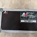 Černý transportní case s kovovými hranami a rohy. Na víku jsou dvě nálepky s logem Audioagency a texty: „Vladimír Urban tel 74-567 230“, „Petr Koudel…