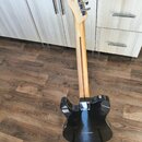Zadní pohled na elektrickou kytaru s černým trupem a světlým dřevěným hmatníkem. Na hlavě nástroje je svisle napsaný nápis "Musicman". Trup vykazuje…