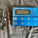 Modrý kytarový syntetizér s nápisem BOSS SY-1000 GUITAR SYNTHESIZER a logem GK v pravém horním rohu. Zařízení má centrální displej, několik ovládacíc…