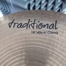 Detailní záběr na kovový činel typu China s koncentrickými rýhami v povrchu. Na povrchu je černým nápisem uveden text traditional a pod ním 16"/40cm…
