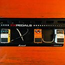 Černý efektový pedalboard značky FXPEDALS s nápisem Marshall na spodní liště. Na desce jsou umístěny tři pedály značky BOSS: modrý Digital Delay DD-3…