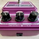 Fialový kytarový efekt s nápisy Maxon Analog Delay a AD-900. Na horní straně jsou tři černé oválné knoflíky s popisky D-LEVEL, REPEAT a D-TIME. V dol…