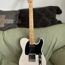 Bílá elektrická kytara typu Telecaster se světle hnědým hmatníkem a černým pickguardem. Na hlavě je viditelné logo Squier. Nástroj vykazuje známky bě…