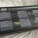Fotografie znázorňuje kartonovou krabici od efektového procesoru. Na víku je velký bílý nápis MG-30 a text VERSATILE MODELER. Krabice obsahuje detail…