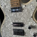 Elektrická kytara v krémové barvě s bílým perleťovým pickguardem. Na obou dvou snímačích je viditelné logo "Gretsch". Kytara má hnědý dřevěný hmatník…