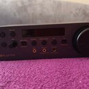 Tmavě šedý audio interface s digitálním displejem a velkým ovládacím knoflíkem vpravo. Na předním panelu je nápis Sound BLASTER a několik tlačítek s…