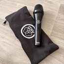 Černý dynamický mikrofon s mřížkou, na těle kterého je nápis AKG P5 S a logo výrobce. Vedle mikrofonu je černý látkový přepravní vak s bílým logem AK…