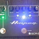 Černý basový předzesilovač s nápisy Ampeg a SCR-DI. Zařízení obsahuje pět otočných ovladačů s popisky Volume, Bass, Mid, Treble a AUX Level, dva přep…