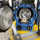 Modrý reflektor s otevřeným předním krytem a čočkou. Uvnitř je viditelná žárovka s nápisem OSRAM, pod ní je text Made in Germany. Na spodní části mod…