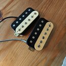Dvě elektrické kytarové snímače typu humbucker s černým tělem a krémovými plastovými kryty. Snímače jsou vybaveny šesti viditelnými poladovacími šrou…