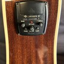 Detail na černý předzesilovač s tunerem vestavěný do hnědého dřevěného korpusu akustické kytary. Na panelu jsou nápisy BASS, TREBLE, PHASE, VOLUME, T…