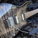 Elektrická kytara s tmavým, pruhovaným povrchem těla v černé barvě. Nástroj má dva humbuckery, chromovaný most s páčkou a hриф z jasného dřeva. Na mo…