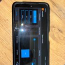 Fotografie zachycuje displej mobilního telefonu v černém pouzdře. Na obrazovce je otevřená aplikace s modrým rozhraním, která obsahuje nápisy „EON 60…