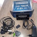 Na fotografii je napájecí zdroj Rockboard ISO Power Block V6 v originální krabici s doprovodným příslušenstvím. Černý zdroj má na horní straně bílý n…