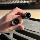 Ruka drží dva černé konektory s kovovými piny. Na obou je v kruhovém nápisu čitelně uvedeno MADE IN GERMANY. Povrch konektorů je hladký a černý.