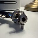 Detailní pohled na kovový mechanismus s černou trubicí. Součásti jsou vyrobeny z anodizovaného hliníku stříbrné barvy a obsahují několik šroubů a uta…