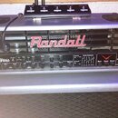 Kytarový zesilovač Randall Ninja v kombinaci s reproduktorovou skříní. Na horním panelu je červené logo Randall a nápis Ninja s doprovodným symbolem.…