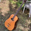 Akustická kytara s přirozenou dřevěnou barvou korpusu a tmavým hnedým hmatníkem. Na hlavě nástroje je viditelný nápis "Cort". Povrch instrumentu vyka…