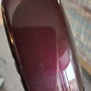 Detailní pohled na tmavě červenou, lakovanou část hudebního nástroje s Rounded hranami. Povrch je vysoce glossy a odráží okolí. Na viditelné části ne…