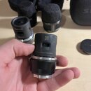 Ruka drží černý mikrofonní modul s kovovým stříbrným kroužkem v dolní části. Na horní části je vyryto „PATS: SHURE.COM/PATENTS“ a umístěn čitelný QR…