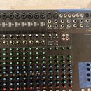 Míčovací pult značky YAMAHA, model MIXING CONSOLE MG16. Zařízení je v tmavě šedé barvě s modrým prvkem v pravé horní části. Povrch obsahuje řadu vstu…