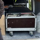 Černý transportní case na kolečkách s kovými hranami a rohy. Na přední straně je vidět značka Kassenova a na horní části jsou nalepené různé nálepy.…