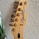 Hlava elektrické kytary z přírodního světlého dřeva se zlatými ladičkami. Na dřevě je černý nápis "Fender" a vedle něj text "TELECASTER". V horní čás…