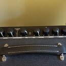 Kytarový kombozesilovač s černým povrchem a koženou rukojetí s bílým prošitím. Na horním ovládacím panelu je nápis FENDER MUSI... INSTRUM... a vpravo…