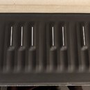 Černý obal z měkkého materiálu s reliéfem připomínajícím klávesy pianina. Na povrchu jsou bílé svislé čárky. Obal nemá žádné viditelné značky ani náp…