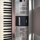 Digitální klavír v stříbrné barvě s bílými a černými klávesami. Na ovládacím panelu je viditelné logo YAMAHA a nápisy STYLE, SONG a VOICE s doprovodn…