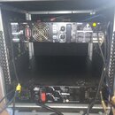Fotografie zachycuje otevřený transportní case s dvěma rackovými zařízeními. Horní zařízení má na zadním panelu nápis INPUT 1, OUTPUT 2 a viditelný v…