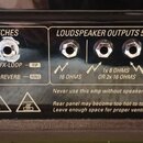 Detail zadní strany zesilovače s černým povrchem. V sekci FOOTSWITCHES jsou dva vstupy s nápisy CHANNEL, 2ND VOLUME, BOOST a FX-LOOP, REVERB. V sekci…