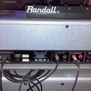 Zadní strana stříbrného kytarového komba značky Randall. Na zadním panelu jsou vidět vstupy a výstupy s nápisy: Footswitch / MIDI, Speaker Outputs, S…