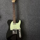 Černá elektrická kytara typu Telecaster s bílým pickguardem a hnědým hmatníkem. Na hlavě kytary je viditelné logo "Ariari". Nástroj vykazuje známky b…