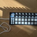 Černý MIDI kontrolér s bílými podsvícenými tlačítky a šeradou otočných knoflíků. Na levé straně je bílý nápis ARTURIA a pod ním text YOUR EXPERIENCE…